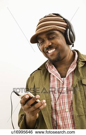 Stock Photograph - Man wearing knit hat and listening to headphones and mp3 player. Fotosearch