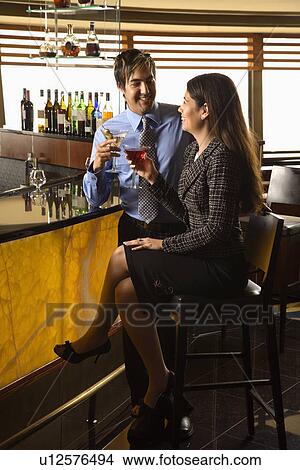 Picture - Mid adult Hispanic couple toasting at bar.. Fotosearch