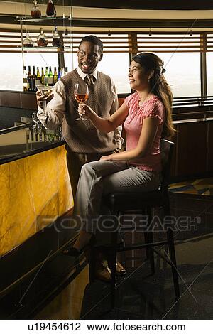 Stock Image - Mid adult man and woman toasting at bar. Fotosearch
