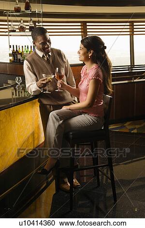 Stock Image - Mid adult man toasting woman at bar. Fotosearch