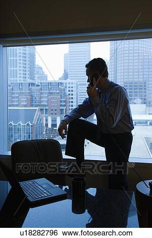 Stock Photograph - Middle-aged Caucasian male in office on phone with skyline in background.. Fotosearch