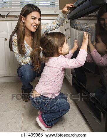 Stock Photography - Mother and daughter kneeling by oven peering in. Fotosearch