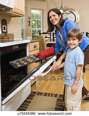 Stock Photography - Mother and son putting cookies into oven. Fotosearch