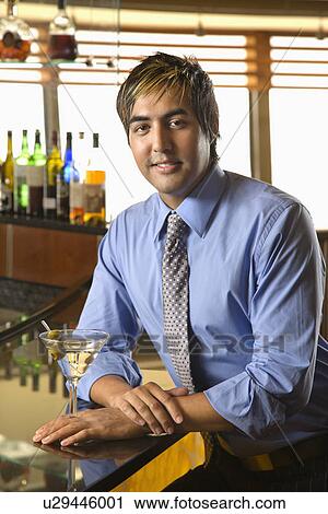 Stock Image - Portrait of Hispanic mid adult man leaning on bar with martini smiling at viewer.. Fotosearch