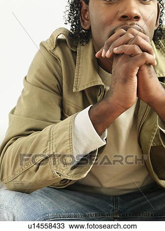 Stock Image - Portrait of man sitting with hands clasped as if in thought.. Fotosearch
