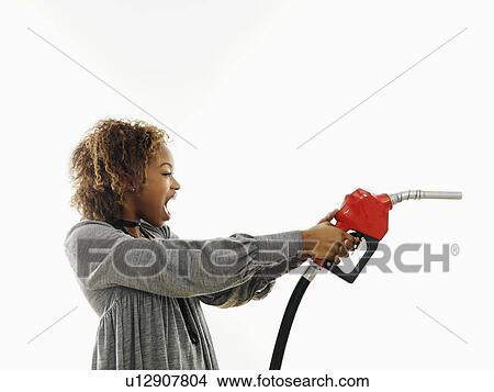 Portrait of pretty young woman holding gas pump nozzle like a gun making angry facial expression on white background. View Large Photo Image Picture - Portrait of pretty young woman holding gas pump nozzle like a gun making angry facial expression on white background.. Fotosearch