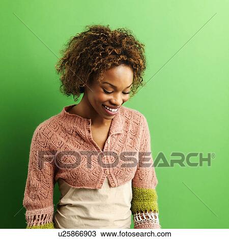 Stock Image - Portrait of pretty young woman standing against green background laughing.. Fotosearch