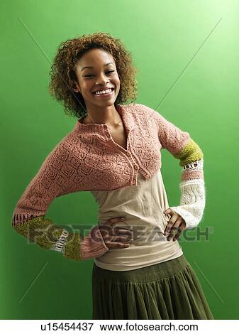 Stock Photo - Portrait of pretty young woman standing against green background with hands on hips smiling.. Fotosearch