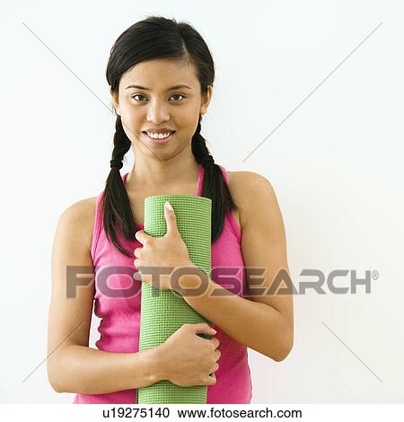 Stock Image - Portrait of smiling young Asian woman holding exercise mat.. Fotosearch