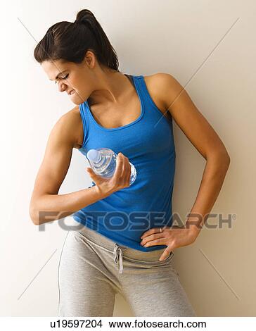 Picture - Portrait of woman in fitness attire flexing arm muscle holding water bottle.. Fotosearch