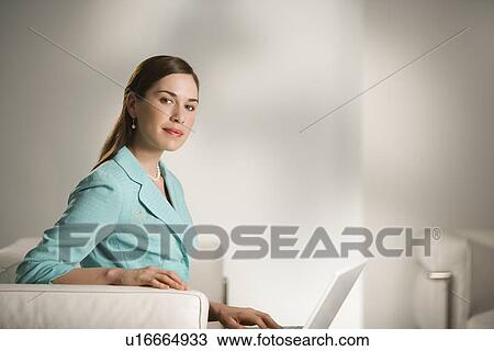 Stock Image - Professional business woman sitting in modern office working on laptop computer looking at viewer. Fotosearch