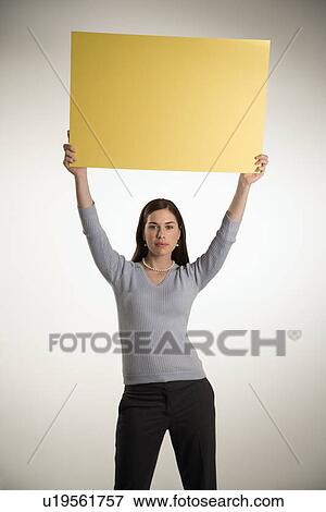 Professional business woman standing holding up blank yellow sign above her head View Large Photo Image Stock Photo - Professional business woman standing holding up blank yellow sign above her head. Fotosearch