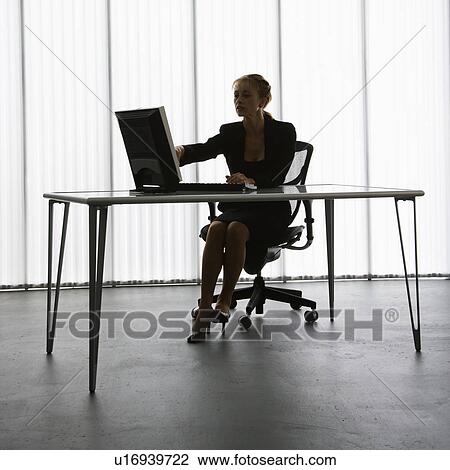 Stock Image - Silhouette of Caucasian businesswoman sitting at desk with computer working.. Fotosearch