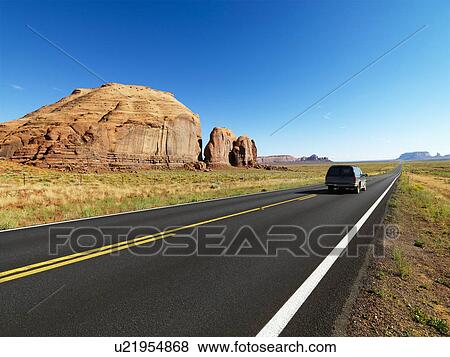 Stock Photo - Sport utility vehicle on open highway in scenic desert landscape with butte land formation. Fotosearch
