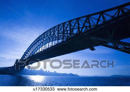 Stock Image - Sydney Harbour Bridge at dusk with view of distant skyline and harbour in Sydney, Australia.. Fotosearch