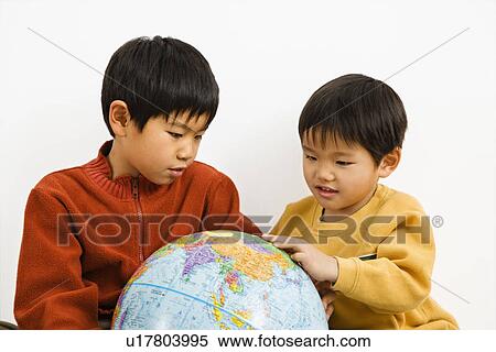 Stock Photography - Two Asian boys looking and pointing at world globe. Fotosearch