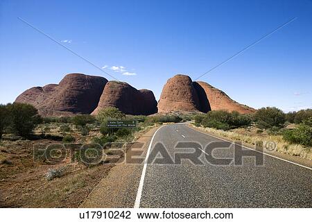 Stock Image - Two lane road in Uluru Kata Tjuta National Park, Australia with Mount Olga in the distance.. Fotosearch