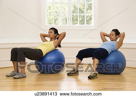 Stock Image - Two young women doing ab workout on balance balls.. Fotosearch