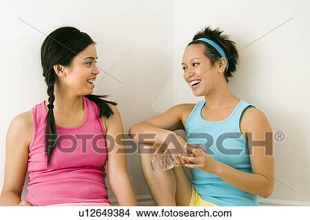 Two young women in fitness clothes sitting smiling and talking. View Large Photo Image Picture - Two young women in fitness clothes sitting smiling and talking.. Fotosearch
