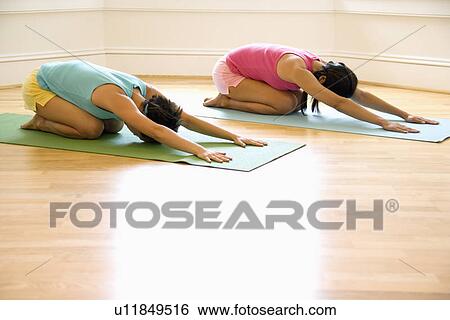 Stock Photograph - Two young women on yoga mats doing child's pose.. Fotosearch