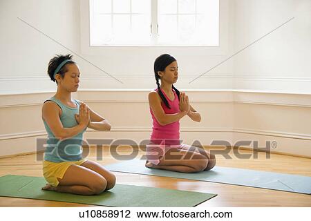 Two young women sitting on yoga mats with eyes closed holding hands in prayer position. View Large Photo Image Stock Image - Two young women sitting on yoga mats with eyes closed holding hands in prayer position.. Fotosearch