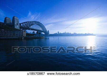 Stock Photo - View of Sydney Harbour with Sydney Harbour bridge and distant skyline at dusk in Sydney, Australia.. Fotosearch