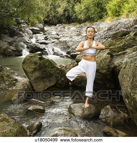 Stock Photo - Woman doing yoga balancing on boulder by creek in Maui, Hawaii. Fotosearch