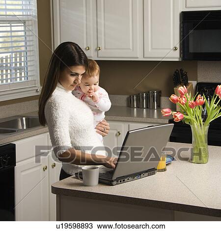 Woman holding baby and typing on laptop computer in kitchen View Large Photo Image Stock Image - Woman holding baby and typing on laptop computer in kitchen. Fotosearch