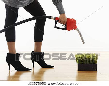 Stock Image - Woman holding gasoline pump nozzle over green grass.. Fotosearch
