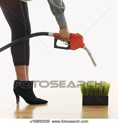 Stock Photo - Woman holding gasoline pump nozzle over green grass. Fotosearch