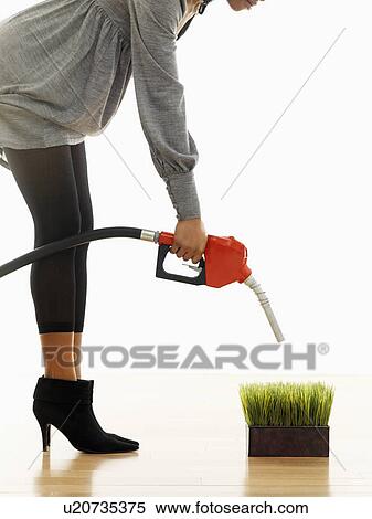 Stock Photography - Woman holding gasoline pump nozzle over green grass.. Fotosearch