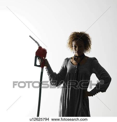 Picture - Woman holding gasoline pump nozzle against white background with dramatic studio lighting.. Fotosearch
