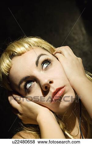 Stock Photo - Woman holding headphones to ears and looking up. Fotosearch