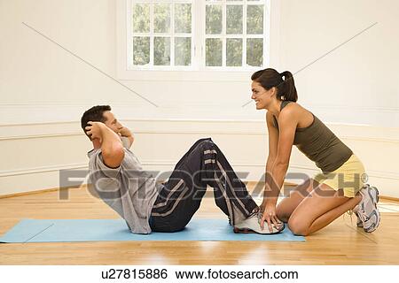 Stock Photograph - Woman holding man's feet down as he does sit up exercises. Fotosearch
