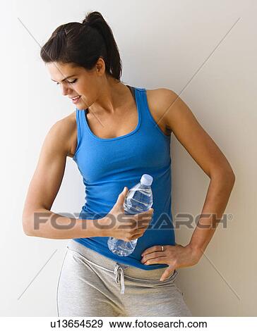 Stock Photo - Woman in fitness attire flexing arm muscle holding bottle and smiling. Fotosearch