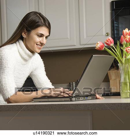 Woman in kitchen looking at laptop computer View Large Photo Image Stock Image - Woman in kitchen looking at laptop computer. Fotosearch
