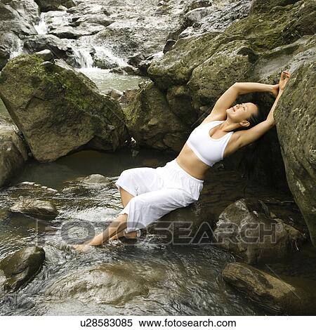 Stock Photography - Woman leaning back on boulder in creek. Fotosearch