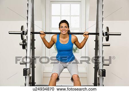 Stock Image - Woman lifting weights in gym smiling.. Fotosearch