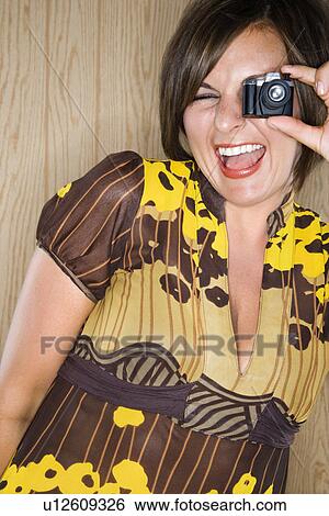 Stock Photograph - Woman looking through miniature toy camera and making facial expression. Fotosearch
