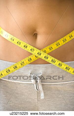 Stock Photography - Woman pulling measuring tape around bare waist.. Fotosearch