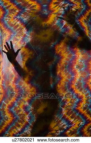 Stock Image - Woman silhouetted behind tye-dye fabric. Fotosearch