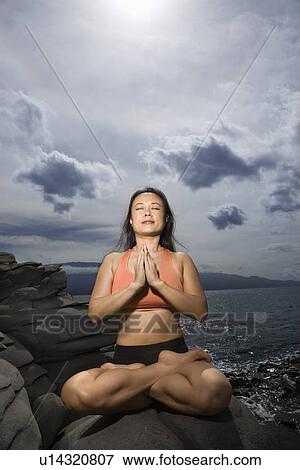 Stock Photo - Woman sitting on rock by ocean in lotus pose with eyes closed in Maui, Hawaii. Fotosearch