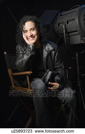 Stock Image - Woman smiling and holding camera in studio setting. Fotosearch
