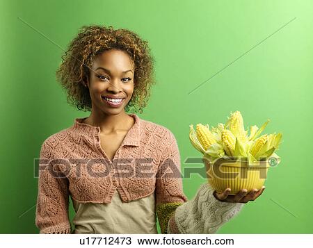 Stock Image - Woman standing holding bowl full of ears of corn. Fotosearch