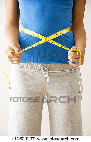 Woman standing pulling measuring tape around waist View Large Photo Image Stock Photo - Woman standing pulling measuring tape around waist. Fotosearch