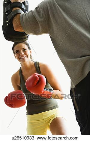 Stock Image - Woman wearing boxing gloves hitting training mitts man is holding. Fotosearch