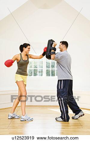 Stock Photo - Woman wearing boxing gloves hitting training mitts man is holding. Fotosearch