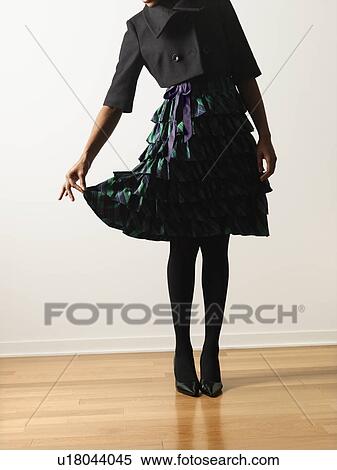 Stock Photography - Woman wearing ruffled dress holding it out daintily with fingers. Fotosearch