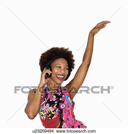 Woman with afro wearing vintage print fabric and listening to headphones smiling and dancing View Large Photo Image Picture - Woman with afro wearing vintage print fabric and listening to headphones smiling and dancing. Fotosearch