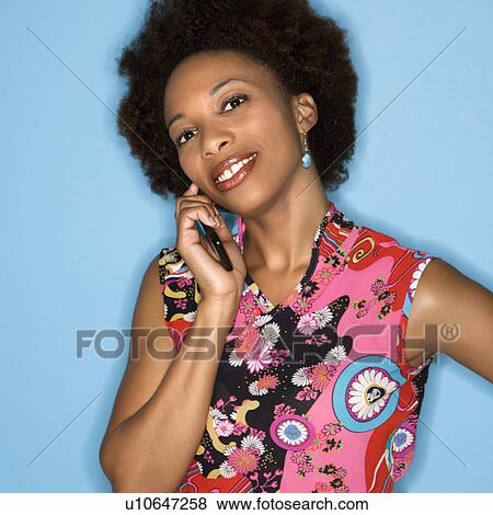 Stock Photo - Woman with afro wearing vintage print fabric smiling holding cellphone. Fotosearch